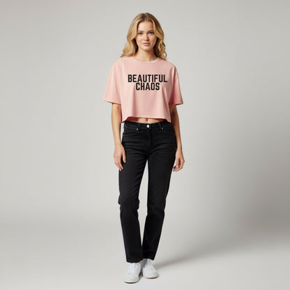 Woman wearing a pink crop top with 'BEAUTIFUL CHAOS' text and black jeans on a light gray background